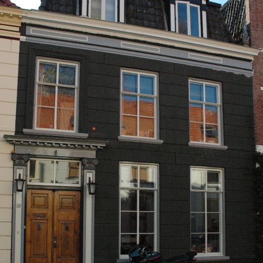 Huis met gepleisterde lijstgevel met composiete kapitelen dragende pilasters ter weerszijden van de deur en schuiframen