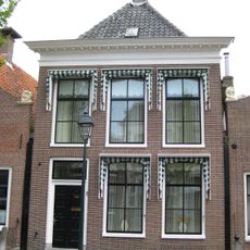 Pand met versierde rechte kroonlijst onder schilddak met hoekschoorstenen