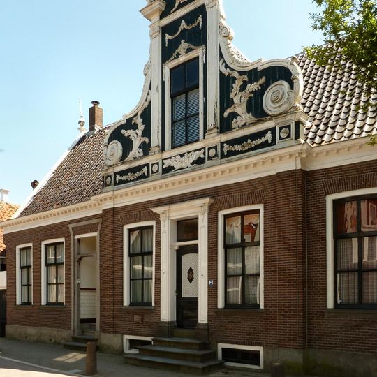 Bakstenen huis, waarvan de brede voorgevel een middenrisaliet heeft, bekroond met een zeer rijk versierd voorschot met Lodewijk XV- en Lodewijk XVI-motieven