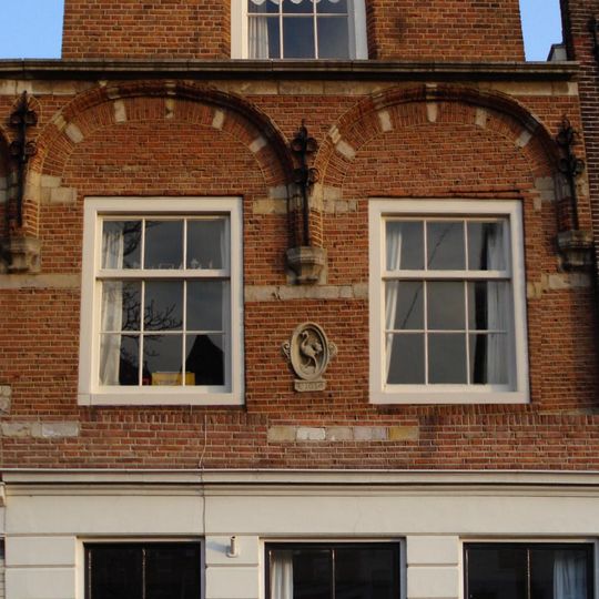 Pand met gepleisterde puntgevel, oorspronkelijk trapgevel met uitgekraagde ontlastingsbogen op kraagsteentjes, geprofileerde puibalk en sierankers