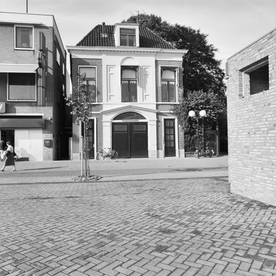 Poortgebouw van twee bouwlagen hoog, drie traveeën breed en gedekt door een met pannen belegd T-vormig schilddak