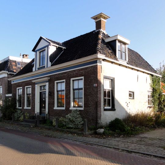 Landelijk woonhuis met omlijste ingang onder schilddak met hoekschoorstenen en forse dakkapel