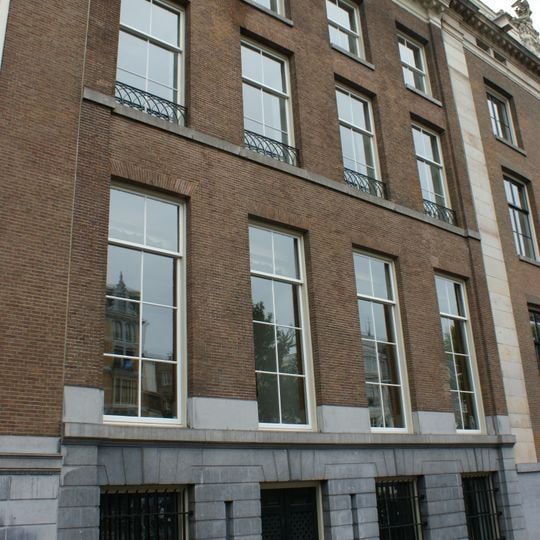 Pand met vier vensters brede gevel met hoeklisenen en lijst waarop balustrade