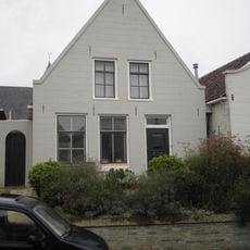 Pand met gepleisterde puntgevel en oude kozijnen met spiegelglas onder zadeldak