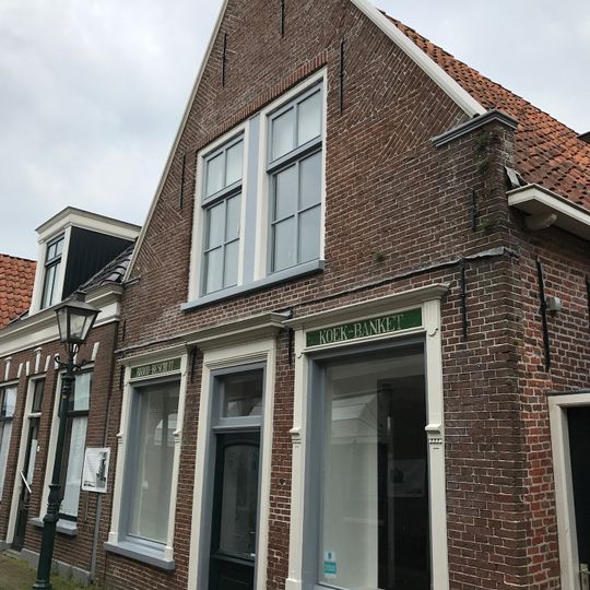 Woning onder zadeldak tegen topgevel met omlijste ingang en vensters en met vlechtingen langs de zijden en opgaand van aanzettreden