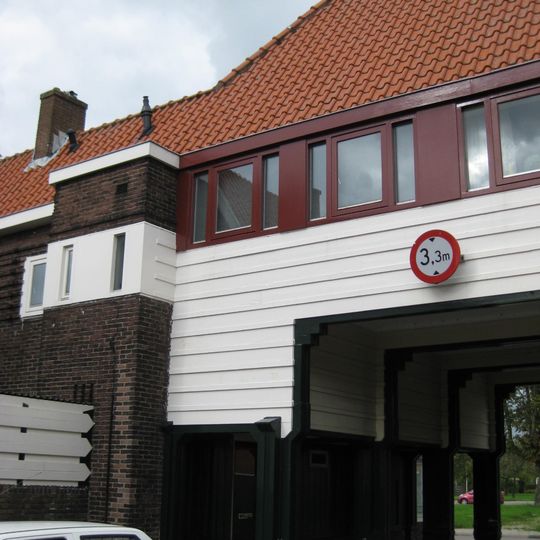 Poortgebouw met twee winkels met bovenwoningen, met veel hout zoals de zware kolommen in poort, bouwstijl Amsterdamse School, ligging aan Purmerweg centraal deel van Tuindorp Nieuwendam